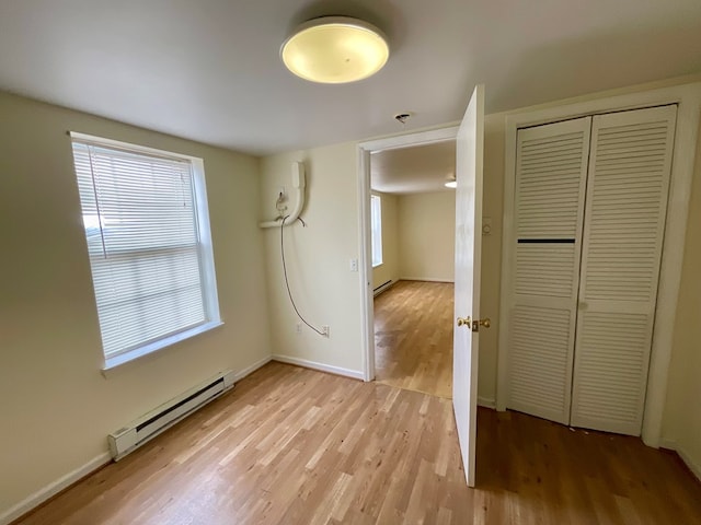 unfurnished bedroom with a baseboard radiator, a closet, baseboards, and light wood-style floors