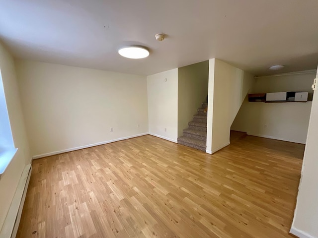 below grade area featuring baseboards, wood finished floors, a baseboard heating unit, and stairway