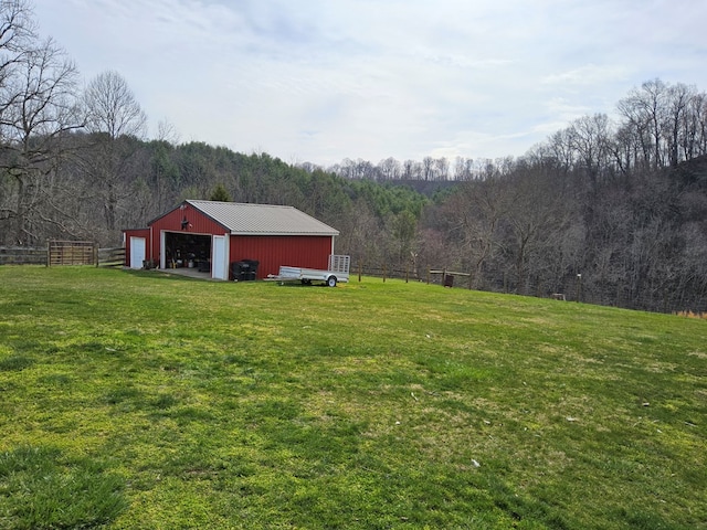 view of yard with a view of trees, an outbuilding, driveway, and fence