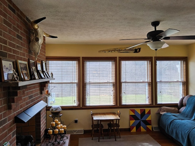 living room featuring a ceiling fan, wood finished floors, a textured ceiling, a brick fireplace, and visible vents