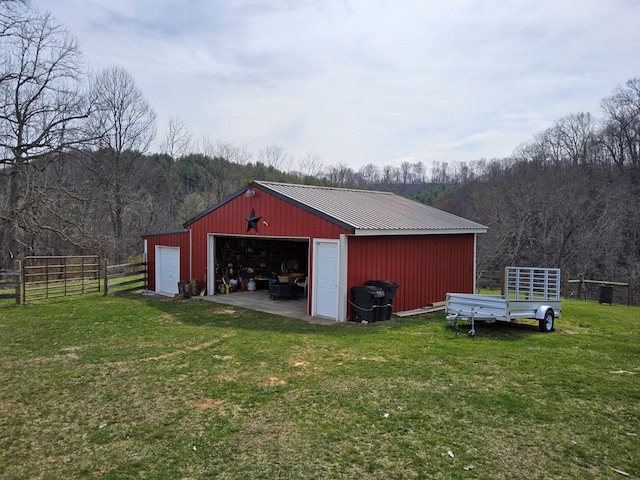 view of pole building with fence, a wooded view, and a yard