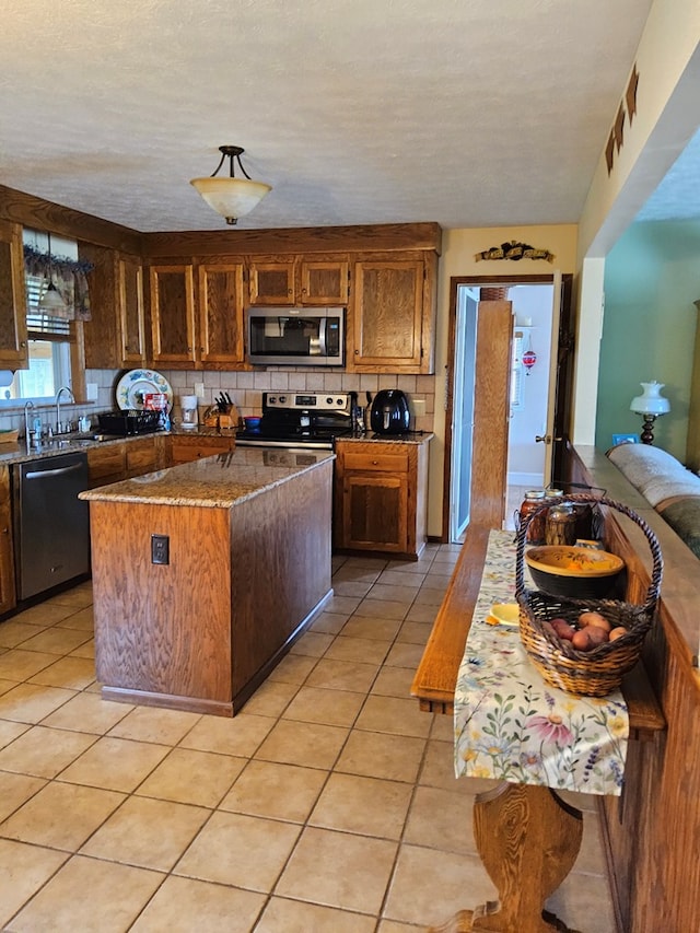kitchen with light tile patterned flooring, stainless steel appliances, a kitchen island, a sink, and backsplash