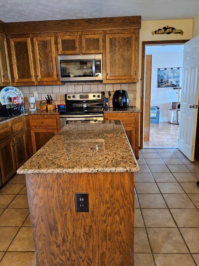 kitchen featuring light tile patterned floors, stainless steel appliances, decorative backsplash, a kitchen island, and light stone countertops