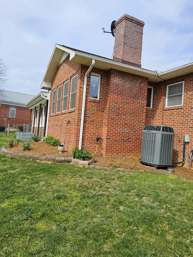 rear view of property featuring brick siding, central AC, a yard, and a chimney