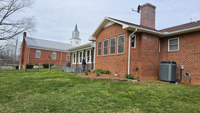 back of house featuring a chimney, fence, brick siding, central AC, and a yard