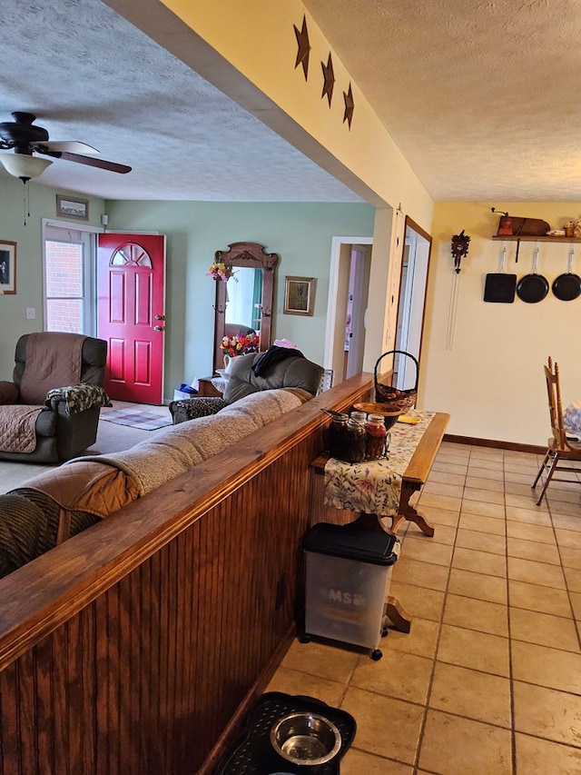 living area with a ceiling fan, light tile patterned floors, baseboards, and a textured ceiling
