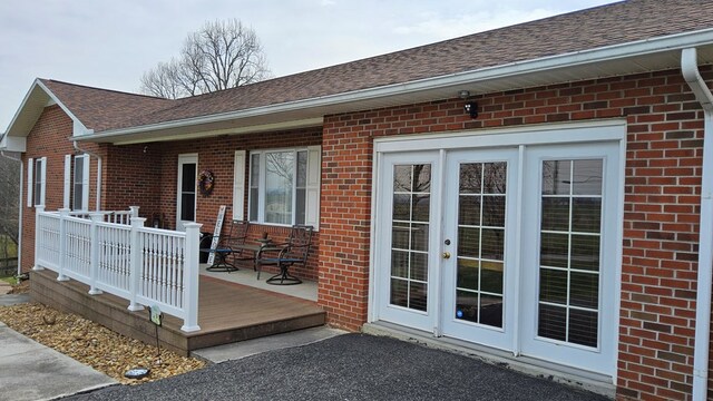 doorway to property featuring brick siding, roof with shingles, and a deck