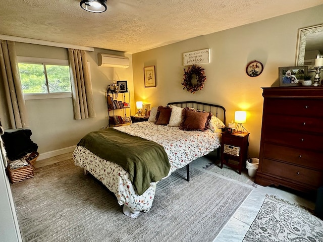 bedroom featuring a wall mounted AC, a textured ceiling, and baseboards