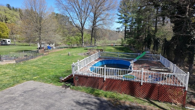 view of yard featuring a fenced in pool, fence, a trampoline, a view of trees, and a deck