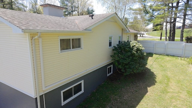 view of home's exterior with a yard, a shingled roof, a chimney, and fence