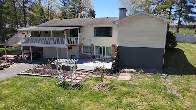 rear view of house with a lawn, stone siding, a chimney, and fence