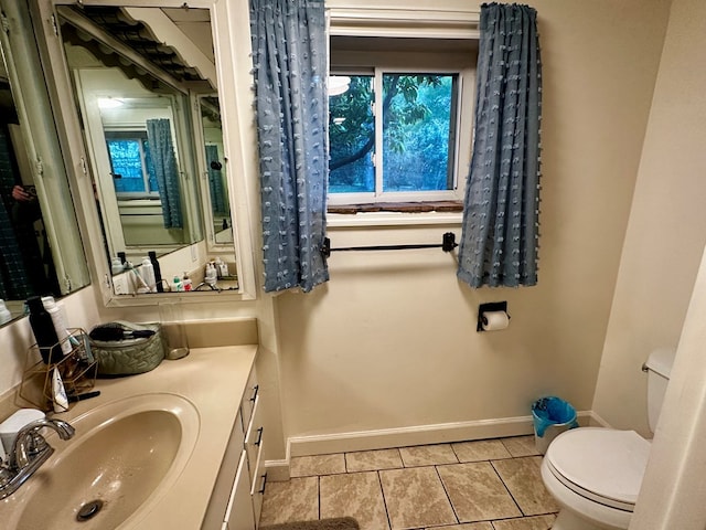 half bathroom featuring tile patterned floors, baseboards, vanity, and toilet