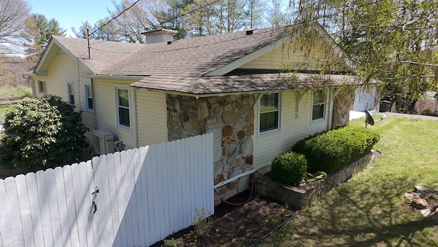 view of property exterior with roof with shingles, stone siding, a chimney, and a lawn