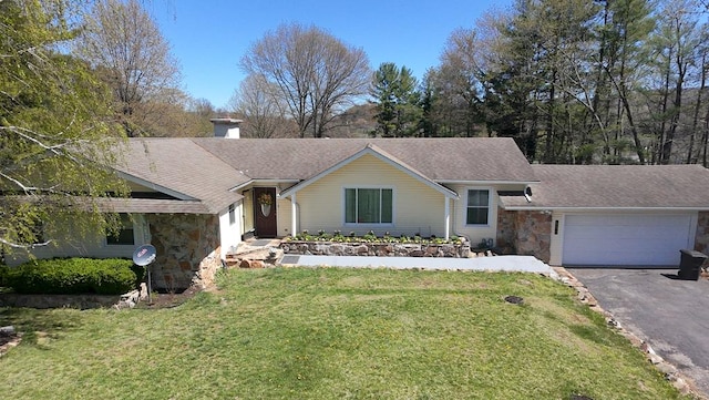ranch-style house with stone siding, a chimney, an attached garage, a front yard, and aphalt driveway