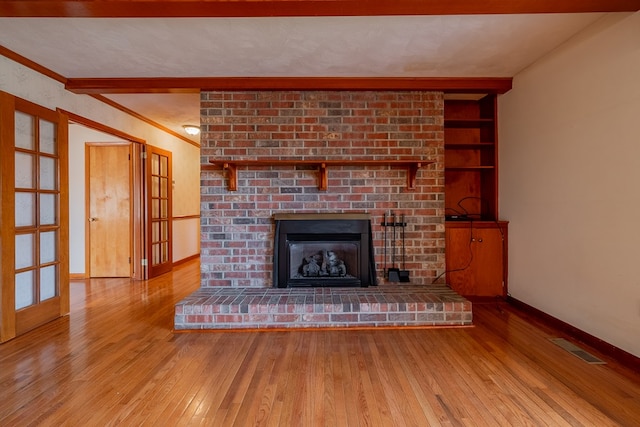 unfurnished living room with visible vents, hardwood / wood-style flooring, crown molding, baseboards, and a brick fireplace