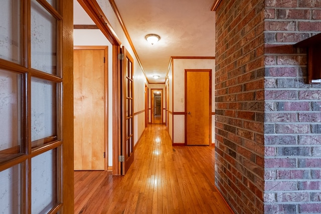 corridor featuring light wood-style flooring, brick wall, and ornamental molding