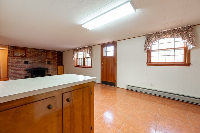 kitchen featuring a baseboard heating unit, brown cabinetry, light countertops, light tile patterned floors, and a brick fireplace