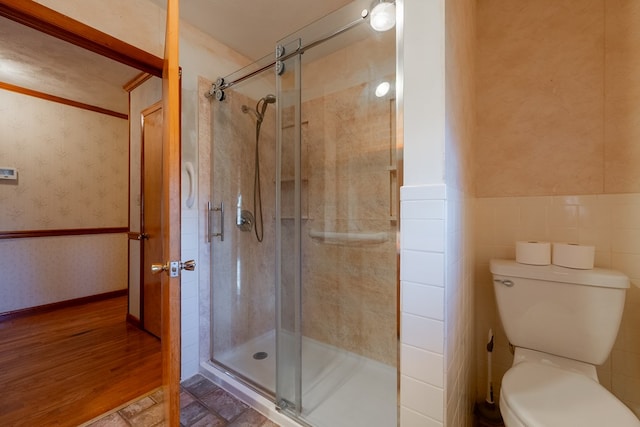 full bath featuring toilet, a stall shower, tile walls, wainscoting, and wallpapered walls