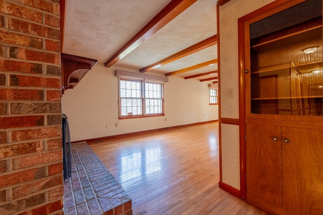 living area with beam ceiling, light wood-style flooring, a textured ceiling, and baseboards