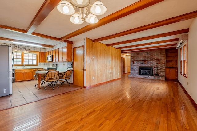 unfurnished living room with light wood finished floors, wooden walls, a chandelier, beam ceiling, and a fireplace