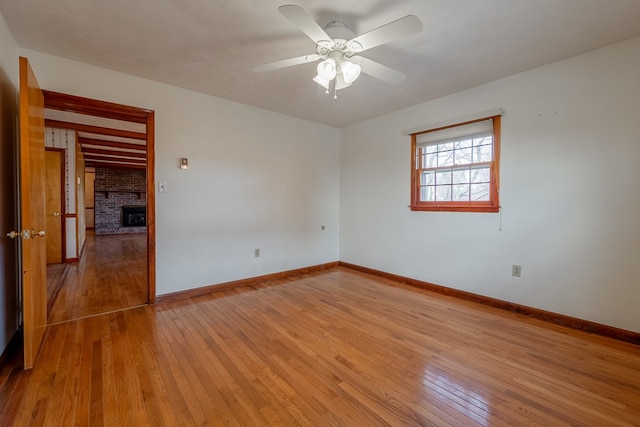 empty room with baseboards, a brick fireplace, ceiling fan, and light wood finished floors