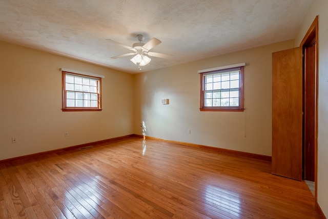 empty room featuring a wealth of natural light, a textured ceiling, a ceiling fan, and light wood finished floors