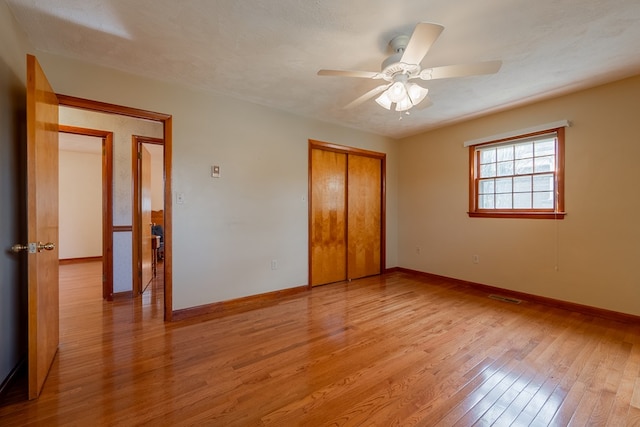 unfurnished bedroom featuring a ceiling fan, visible vents, baseboards, light wood-style flooring, and a closet