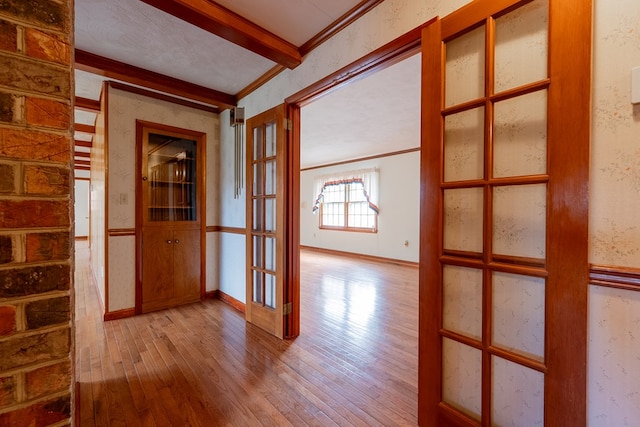 unfurnished room with baseboards, ornamental molding, beam ceiling, hardwood / wood-style floors, and french doors