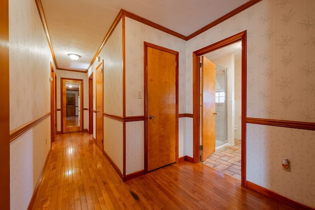 hall featuring a wainscoted wall, wood-type flooring, ornamental molding, and wallpapered walls