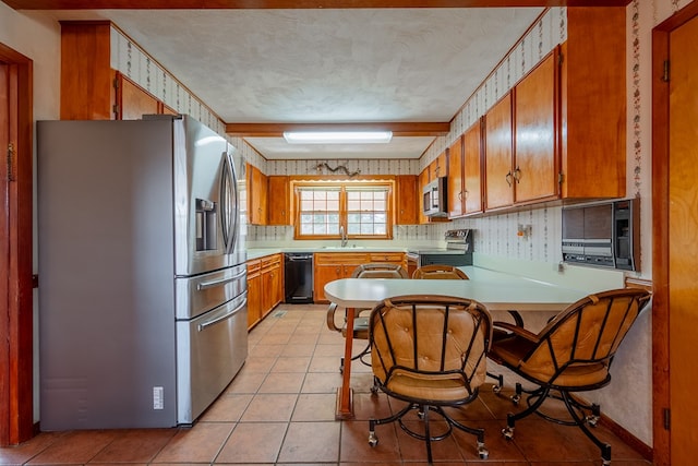 kitchen featuring a sink, appliances with stainless steel finishes, brown cabinetry, and light tile patterned floors