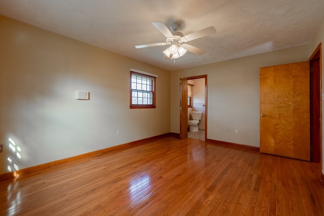 unfurnished bedroom with connected bathroom, baseboards, light wood-style floors, a textured ceiling, and a ceiling fan