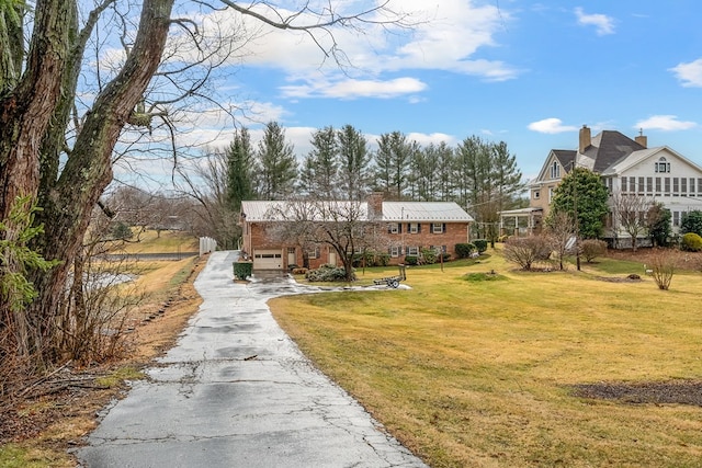 view of front of property with aphalt driveway, an attached garage, a front yard, brick siding, and a chimney