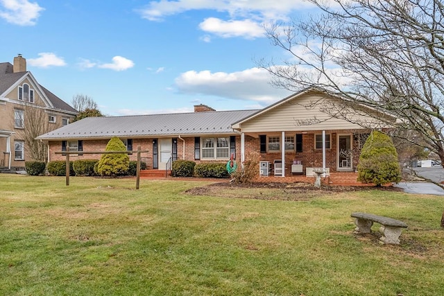 single story home with a front yard, covered porch, a chimney, brick siding, and metal roof