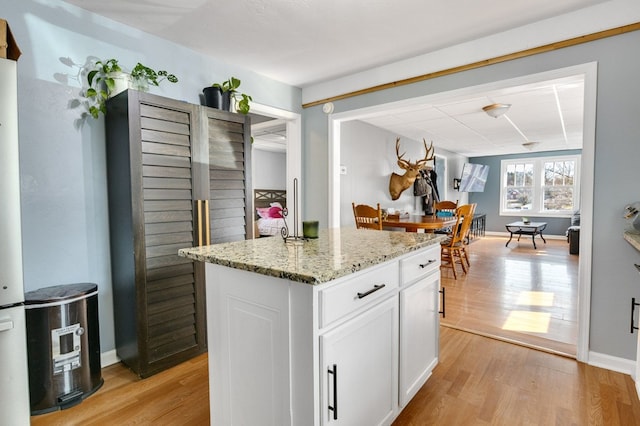 kitchen featuring a kitchen island, baseboards, light stone countertops, light wood-style floors, and white cabinetry