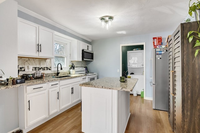 kitchen with light wood-style flooring, stacked washer and clothes dryer, stainless steel appliances, and a sink