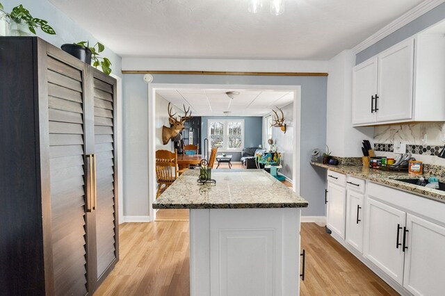 kitchen featuring light stone countertops, white cabinets, light wood-style floors, backsplash, and a center island