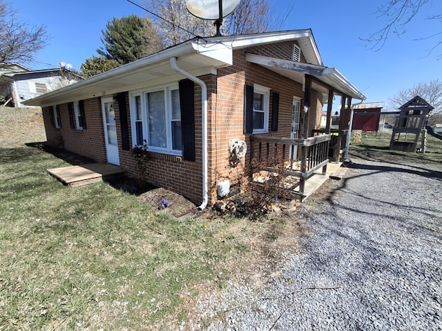 view of side of property with covered porch, a yard, and brick siding