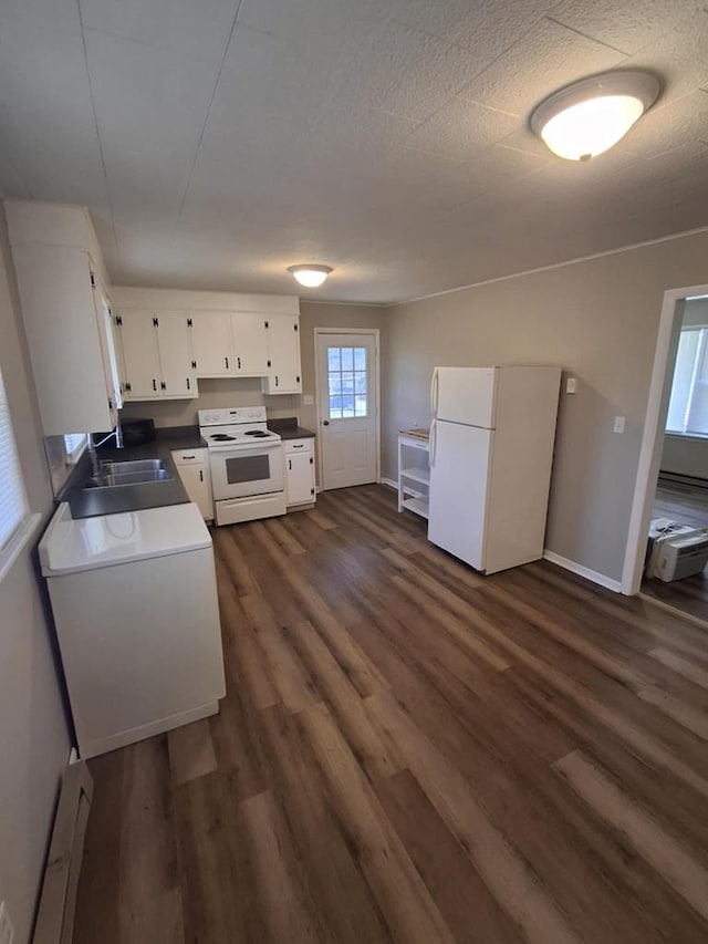 kitchen featuring dark wood-style flooring, a sink, baseboards, white cabinets, and white appliances