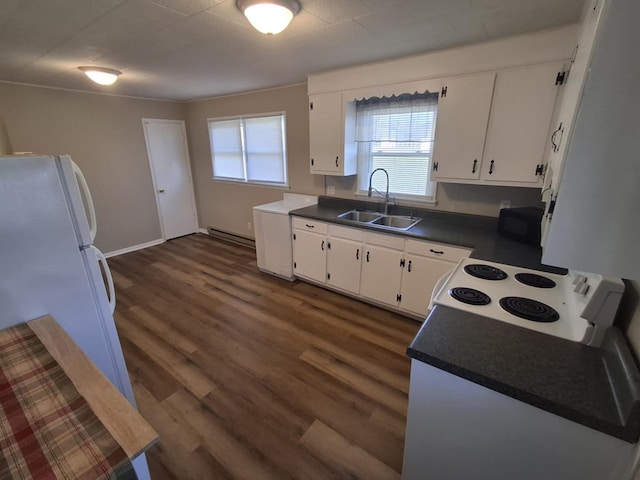 kitchen with dark countertops, a sink, white appliances, plenty of natural light, and white cabinetry