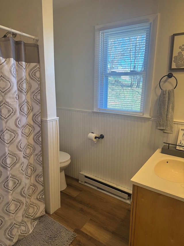 bathroom featuring a wainscoted wall, plenty of natural light, a baseboard heating unit, and toilet