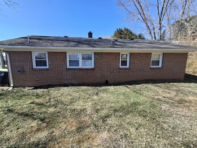 view of side of home with brick siding, a shingled roof, a yard, and a chimney