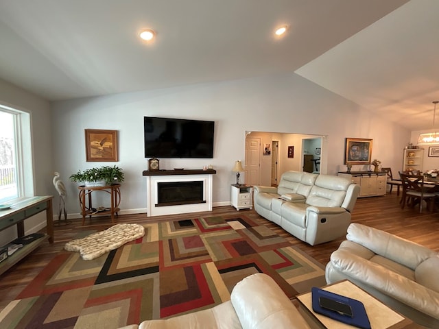 living area with an inviting chandelier, a glass covered fireplace, baseboards, wood finished floors, and vaulted ceiling