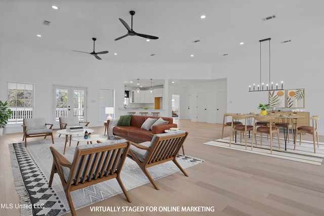 living room with light hardwood / wood-style flooring, ceiling fan with notable chandelier, and a towering ceiling