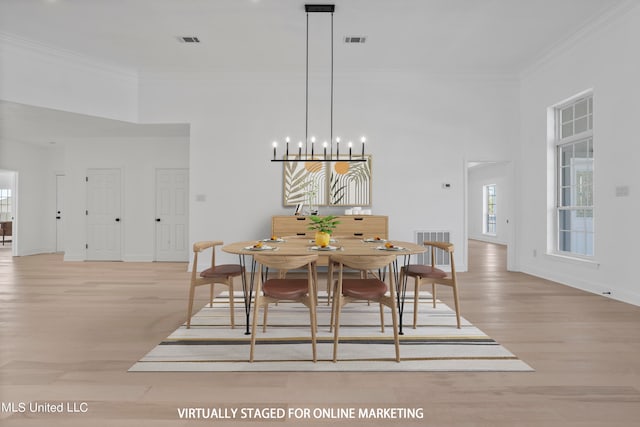 dining room with a notable chandelier, ornamental molding, a high ceiling, and light wood-type flooring