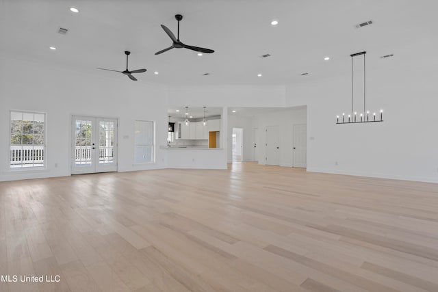 unfurnished living room with light hardwood / wood-style flooring, a chandelier, and a high ceiling