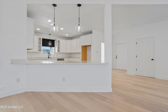 kitchen with white cabinets, kitchen peninsula, decorative light fixtures, and light wood-type flooring