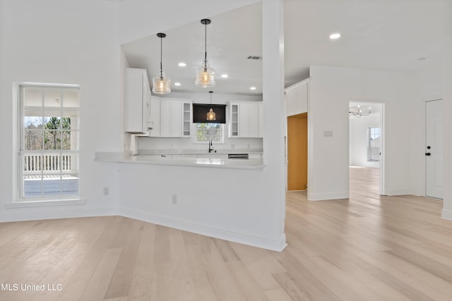 kitchen featuring light hardwood / wood-style flooring, kitchen peninsula, sink, pendant lighting, and white cabinets