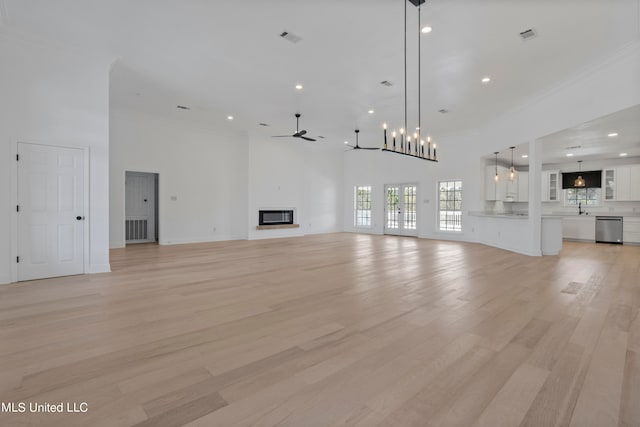 unfurnished living room featuring sink, light wood-type flooring, ceiling fan with notable chandelier, a high ceiling, and ornamental molding