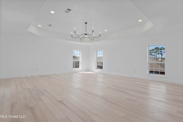 empty room featuring light hardwood / wood-style flooring, a chandelier, and a tray ceiling