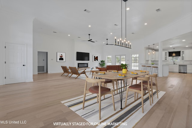 dining space with a towering ceiling, sink, light wood-type flooring, ceiling fan with notable chandelier, and crown molding